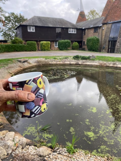 A mug of tea beside a round pond in front of an oast house
